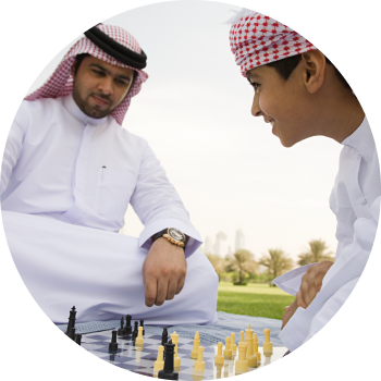 Young man and a boy in white thobe playing chess, focused on developing strategic thinking skills.
